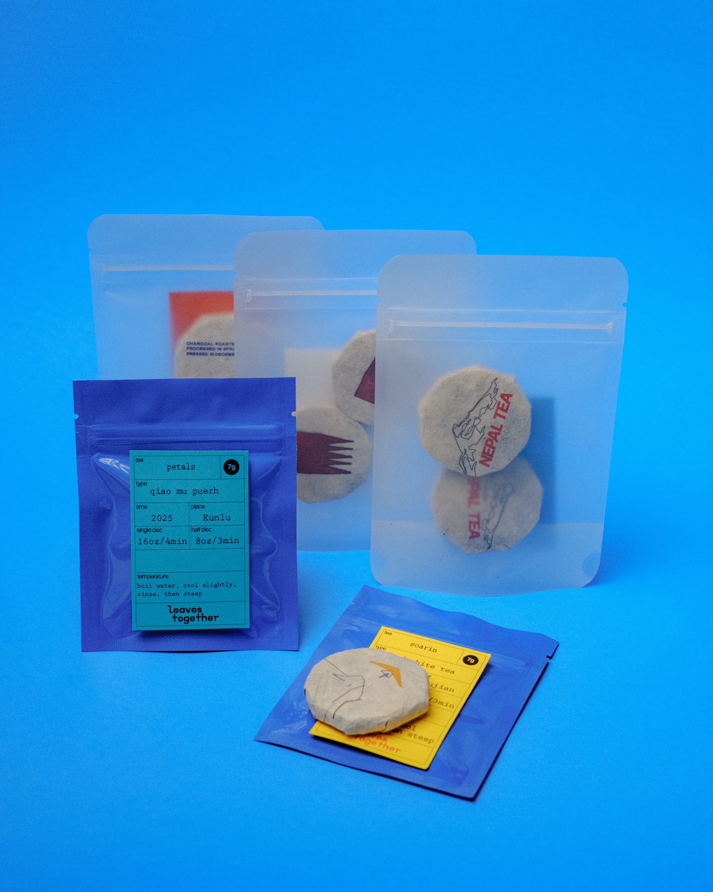Assorted tea samples in clear bags and blue mylar pouch on a blue background.