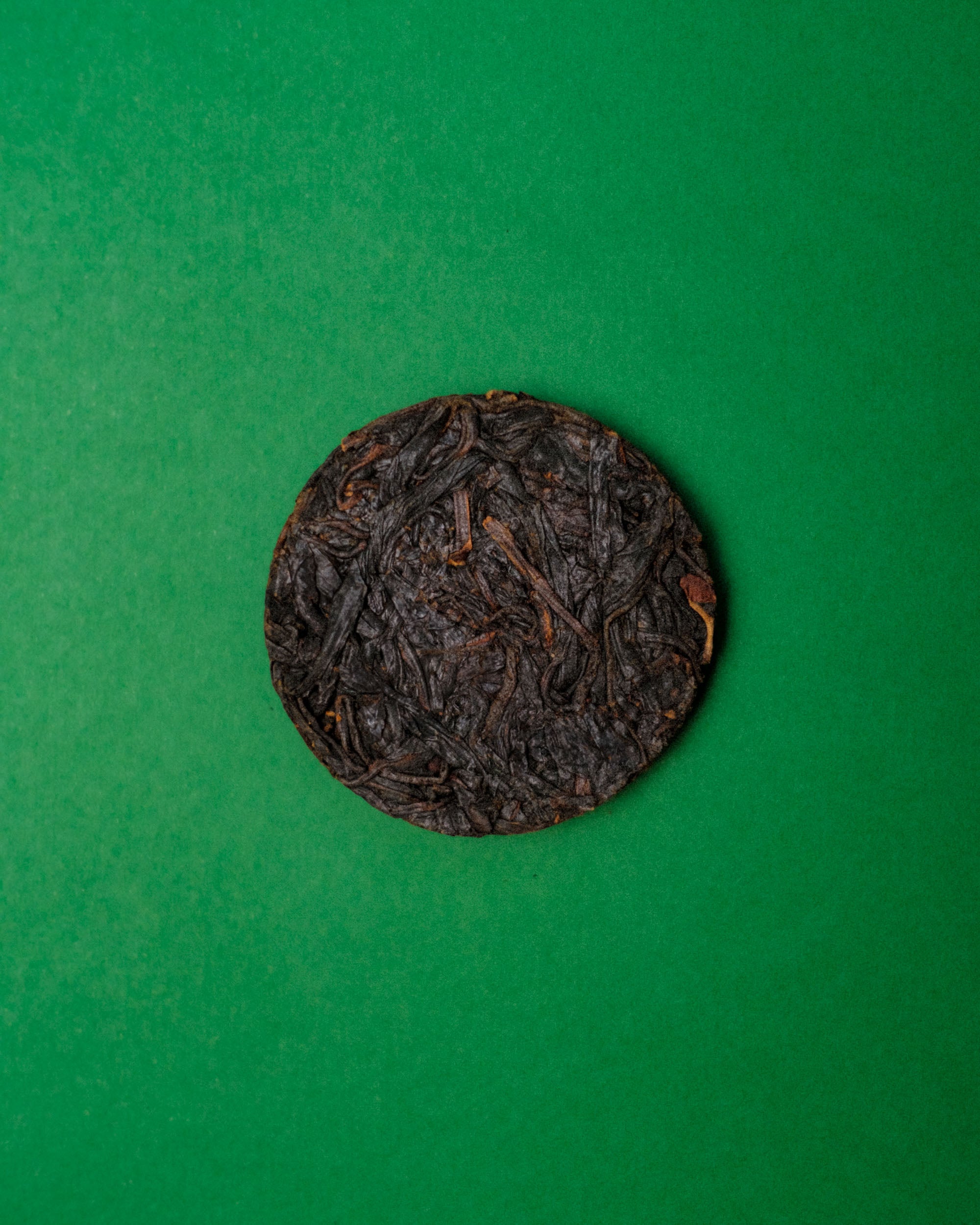 A circular dark reddish brown compressed tea disc centered on a solid green background.