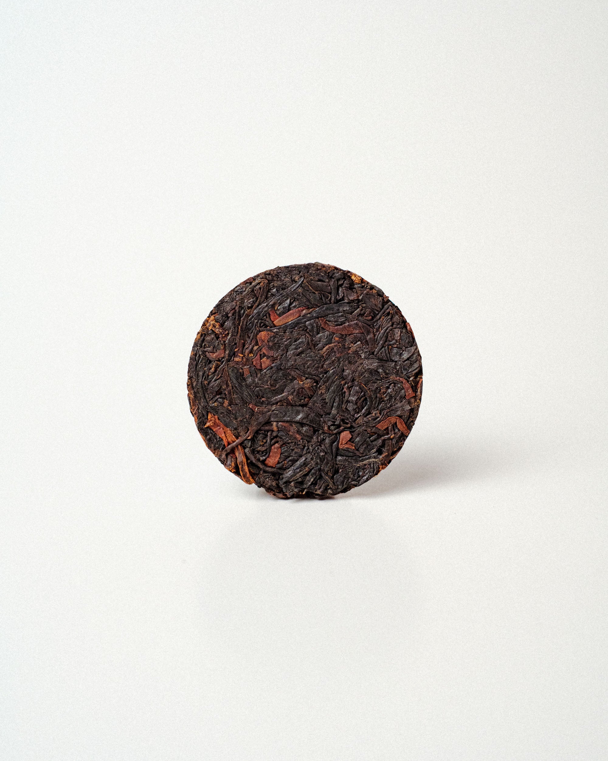 A circular compressed cake of dark reddish brown tea leaves photographed on a clean white background.