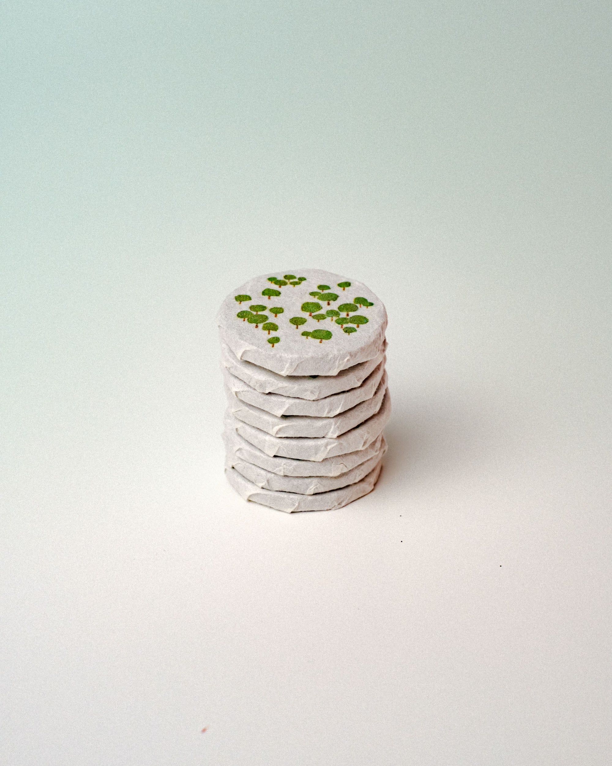A small stack of round tea discs, with several green tree drawings on the top piece, photographed against a plain light background.